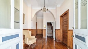 A hallway with wooden flooring, a chandelier, and a staircase leading to another level. - Victorian Manor: Downtown Apt, near Silver Springs & Fort King Historic Park (Ocala)