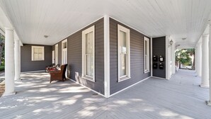 A covered porch with a white ceiling and grey siding, featuring a bench and a table. - Victorian Manor: Downtown Apt, near Silver Springs & Fort King Historic Park (Ocala)