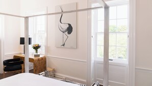 Un dormitorio con cama con dosel, un escritorio con lámpara, una silla y una obra de arte en la pared de un pájaro.
