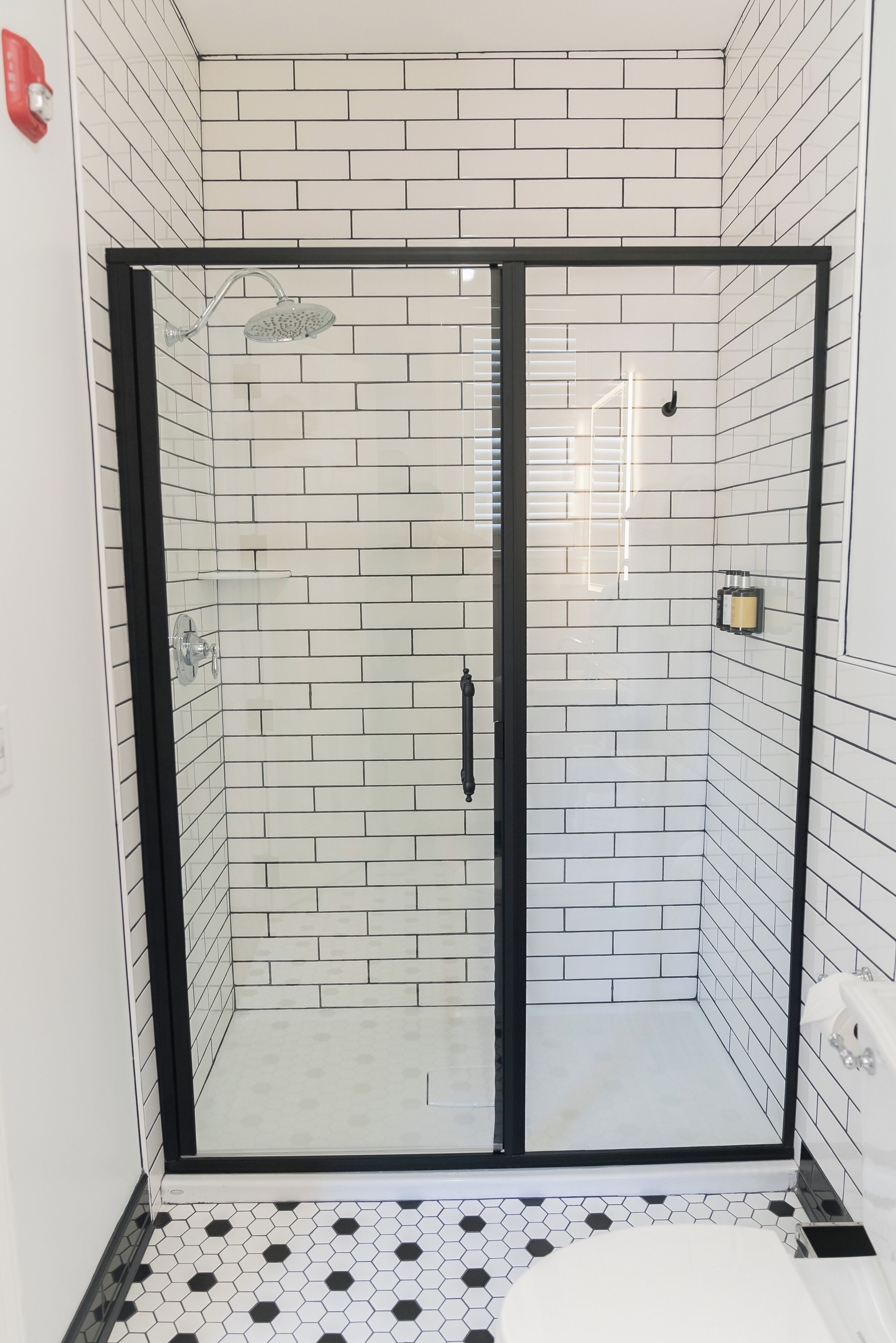 Een douche met glazen deur, witte betegelde wanden en een zwarte vloer.