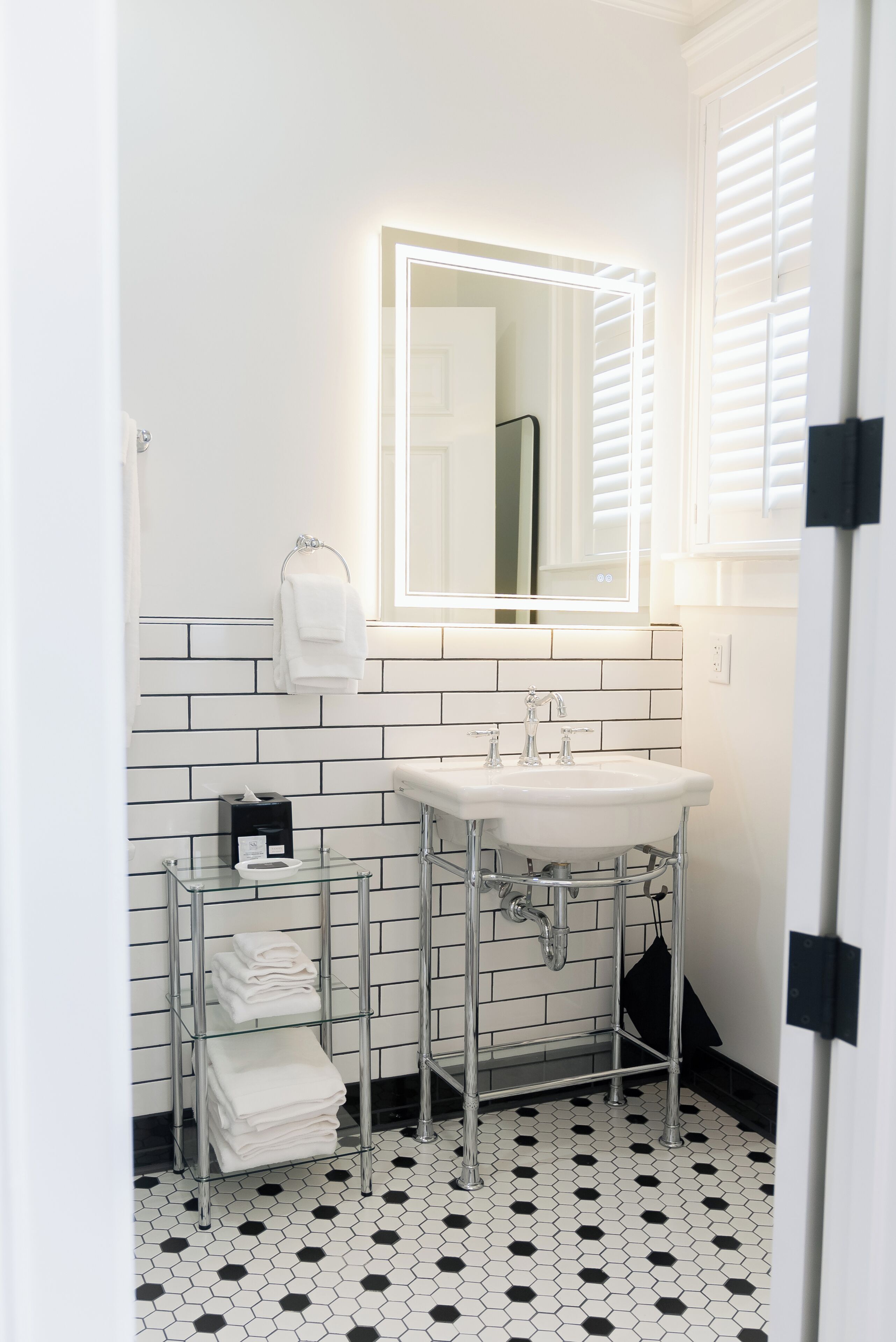 Un baño con lavamanos blanco, un espejo y un perchero para toallas.