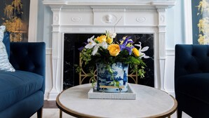 Una habitación con chimenea, dos sofás azules, una mesa de centro redonda y arreglos florales.