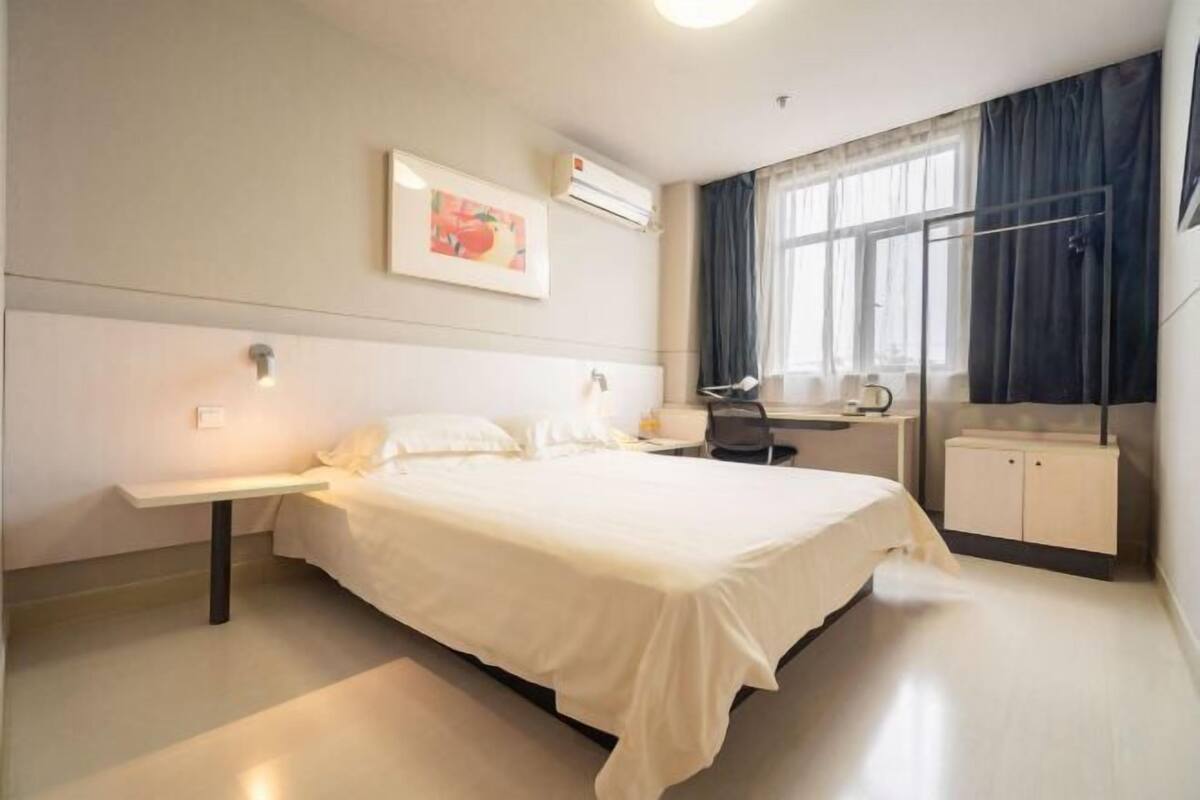 A hotel room with a bed, bedside table, desk, chair, and a wardrobe.