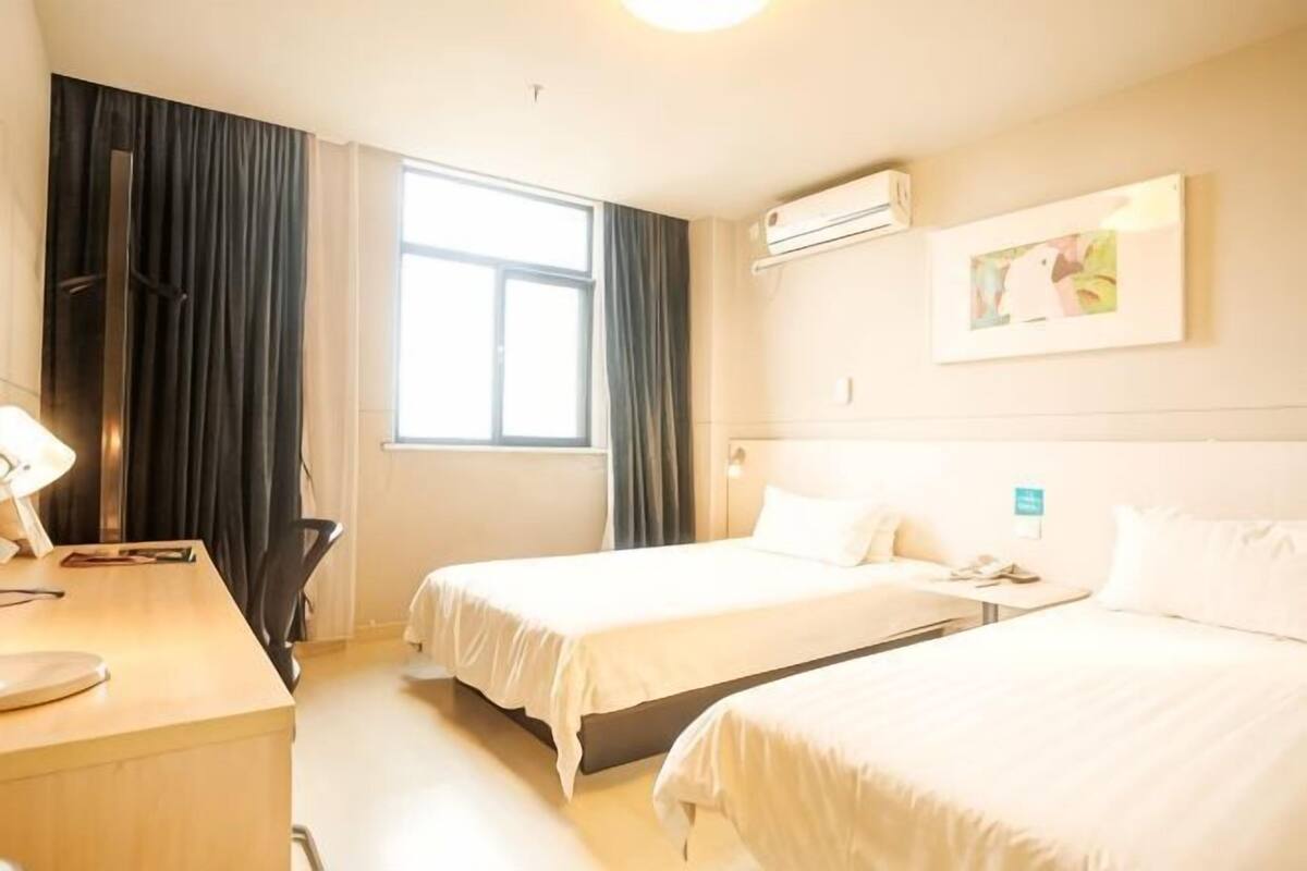A hotel room with two beds, a desk, a chair, and a window with curtains.