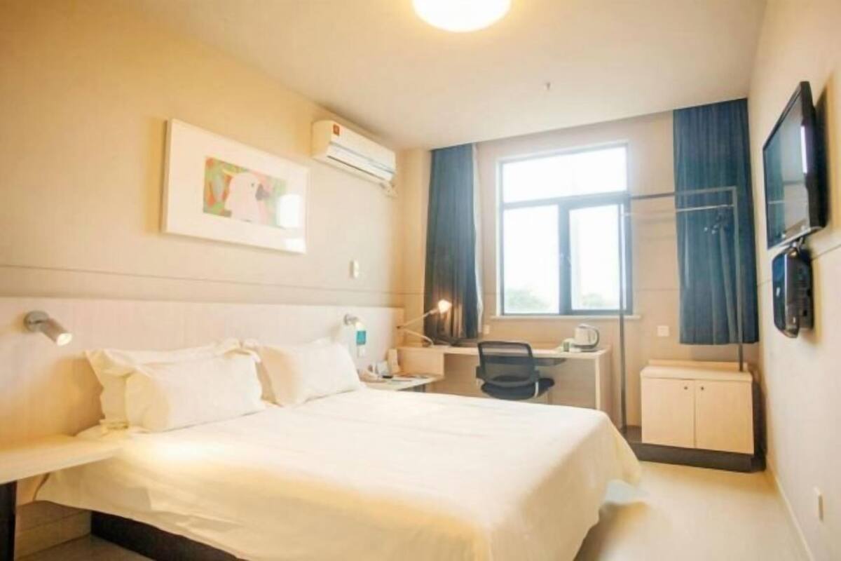 A hotel room with a bed, desk, chair, TV, and a window.