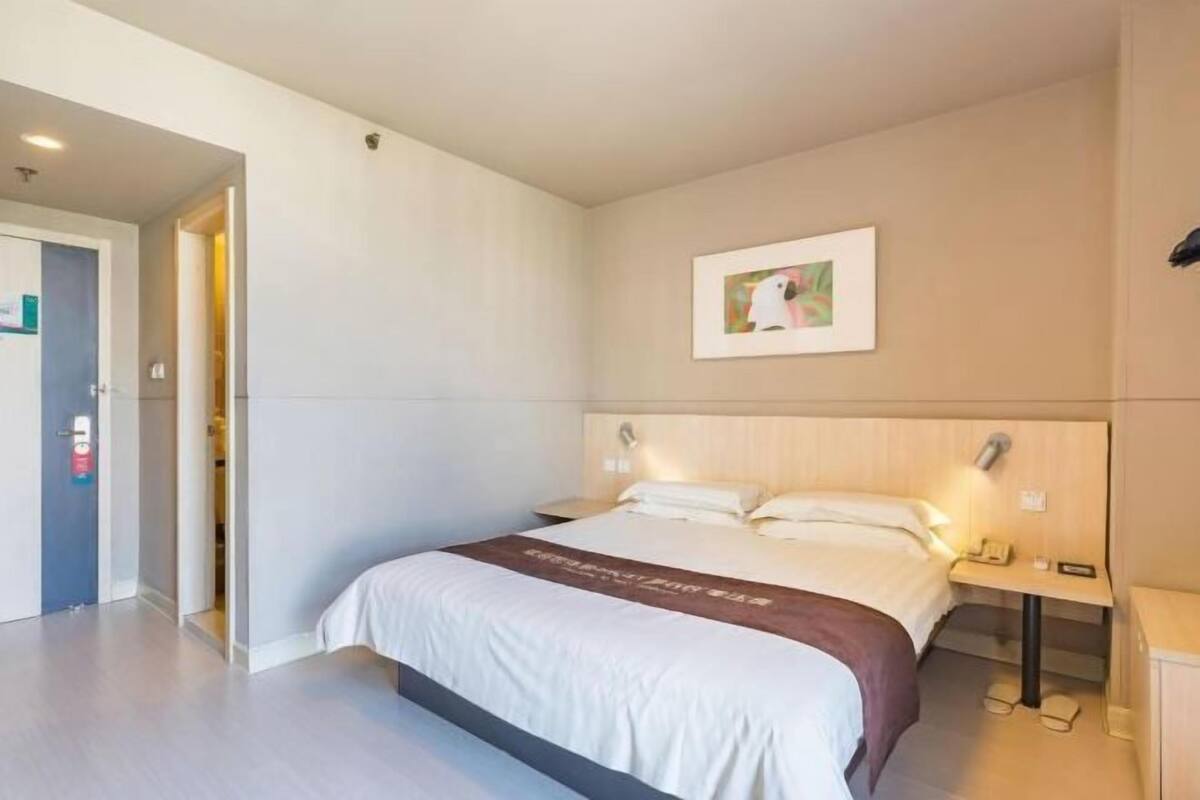 A hotel room with a bed, bedside table, and a framed picture on the wall.