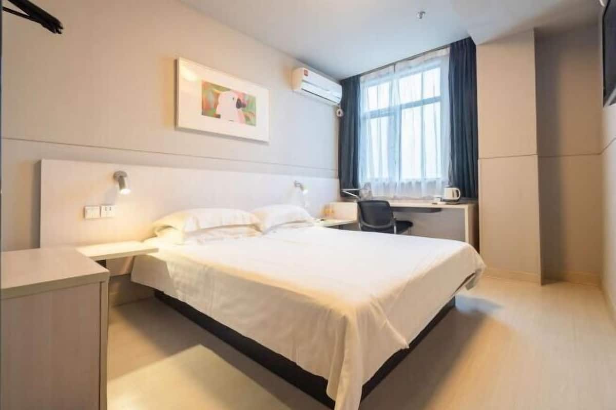 A hotel room with a bed, bedside table, desk, chair, and a window with curtains.