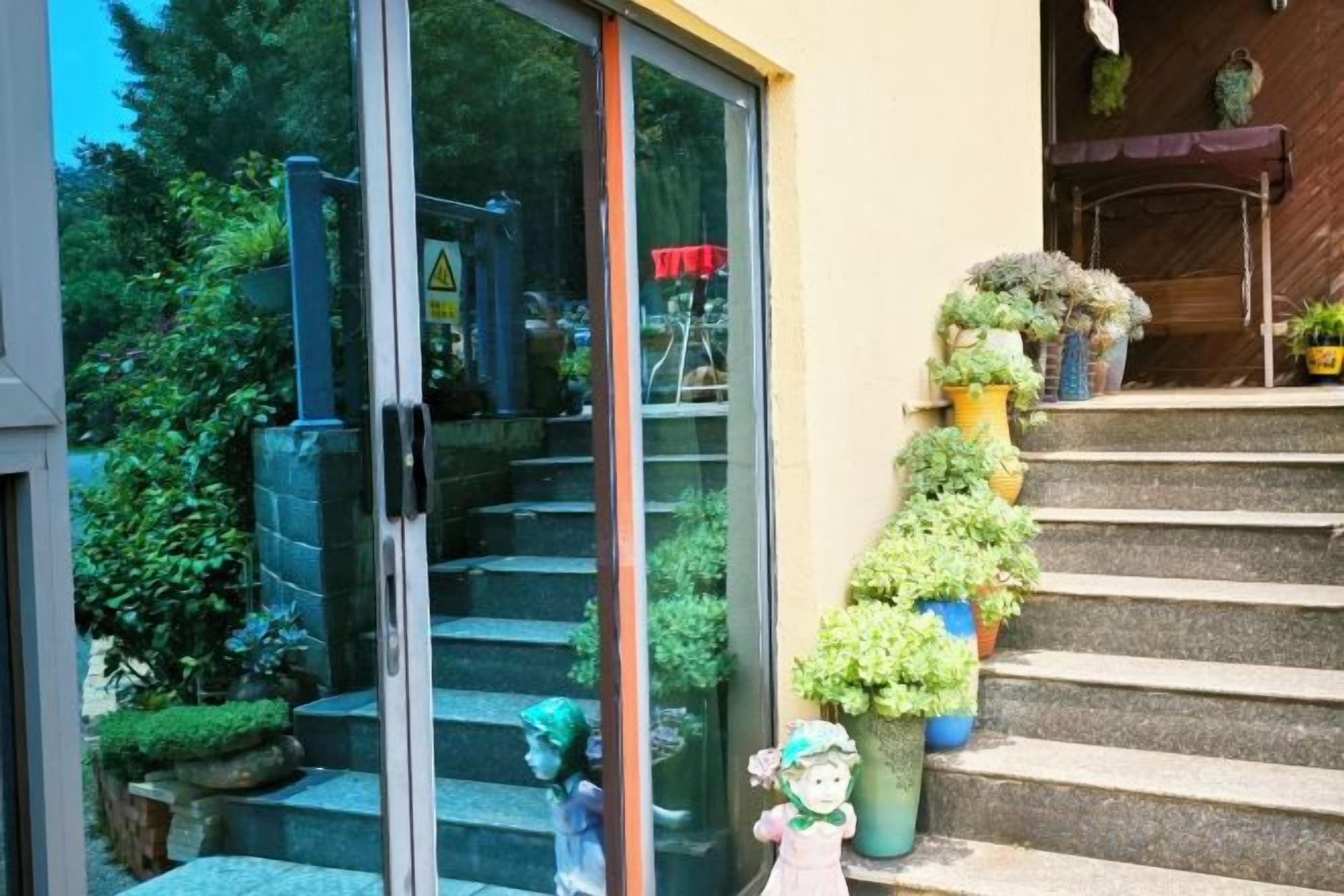 Entrada de un edificio con puerta de vidrio, escalones y plantas en macetas.