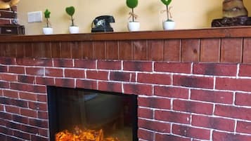 Una chimenea de ladrillo con fuego, un repisa de madera con pequeñas macetas, y un enchufe en la pared.