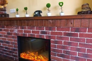 A brick fireplace with a fire, a wooden mantel with small potted plants, and a wall outlet above.