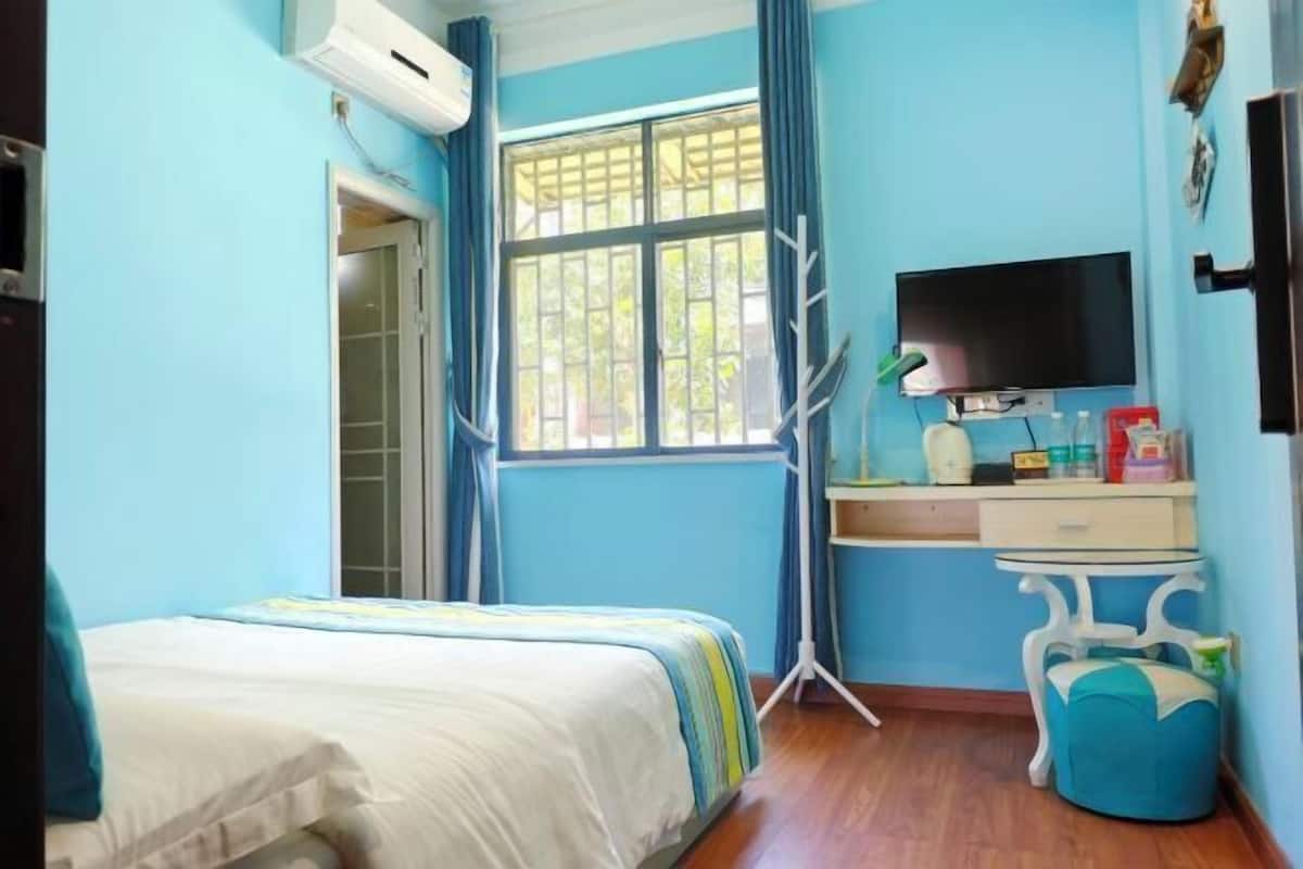 A bedroom with a bed, a desk, a television, and a window with curtains.