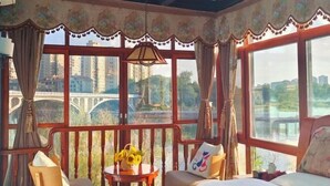 Une chambre avec un lit, une petite table sur laquelle est posé un vase de fleurs, une chaise et une vue sur un pont et une rivière.