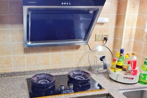 Una cocina con microondas integrado, dos hornillas a gas y una encimera con diversos utensilios de cocina.