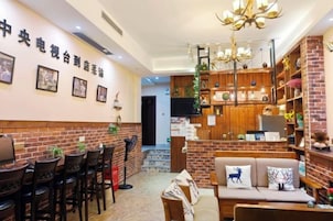 Un vestíbulo de hotel con pared de ladrillo, una recepción, una zona de estar con sofá y sillones, y un candelabro.