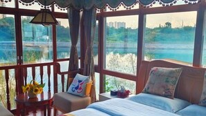 Une pièce comprenant un lit, une chaise, une table ornée d’un vase de tournesols et de grandes fenêtres donnant sur une étendue d’eau.