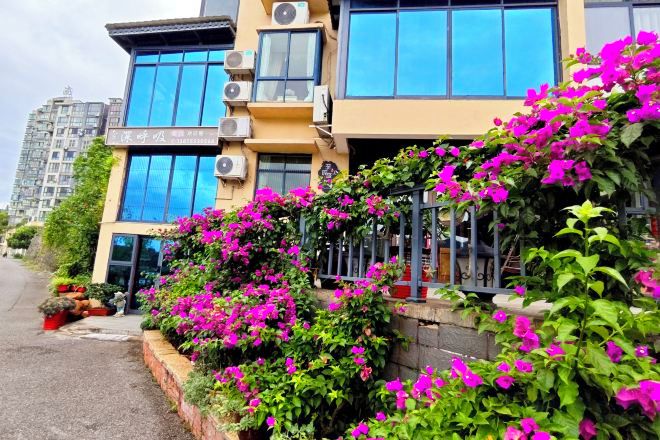 A building with a yellow facade, large windows, and a balcony with pink flowers.