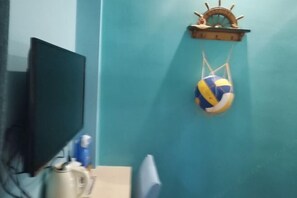 A room with a teal wall, a television, a coffee maker, and a volleyball on a shelf. - Deep Breathe Inn (Zixing)