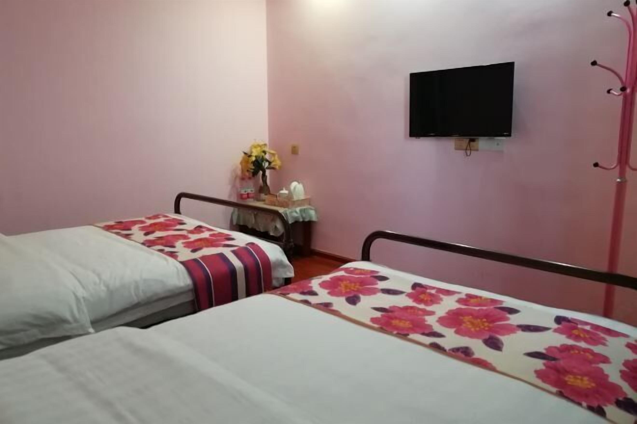 Habitación con dos camas, un televisor de pantalla plana en la pared y una pequeña mesa con un jarrón de flores.