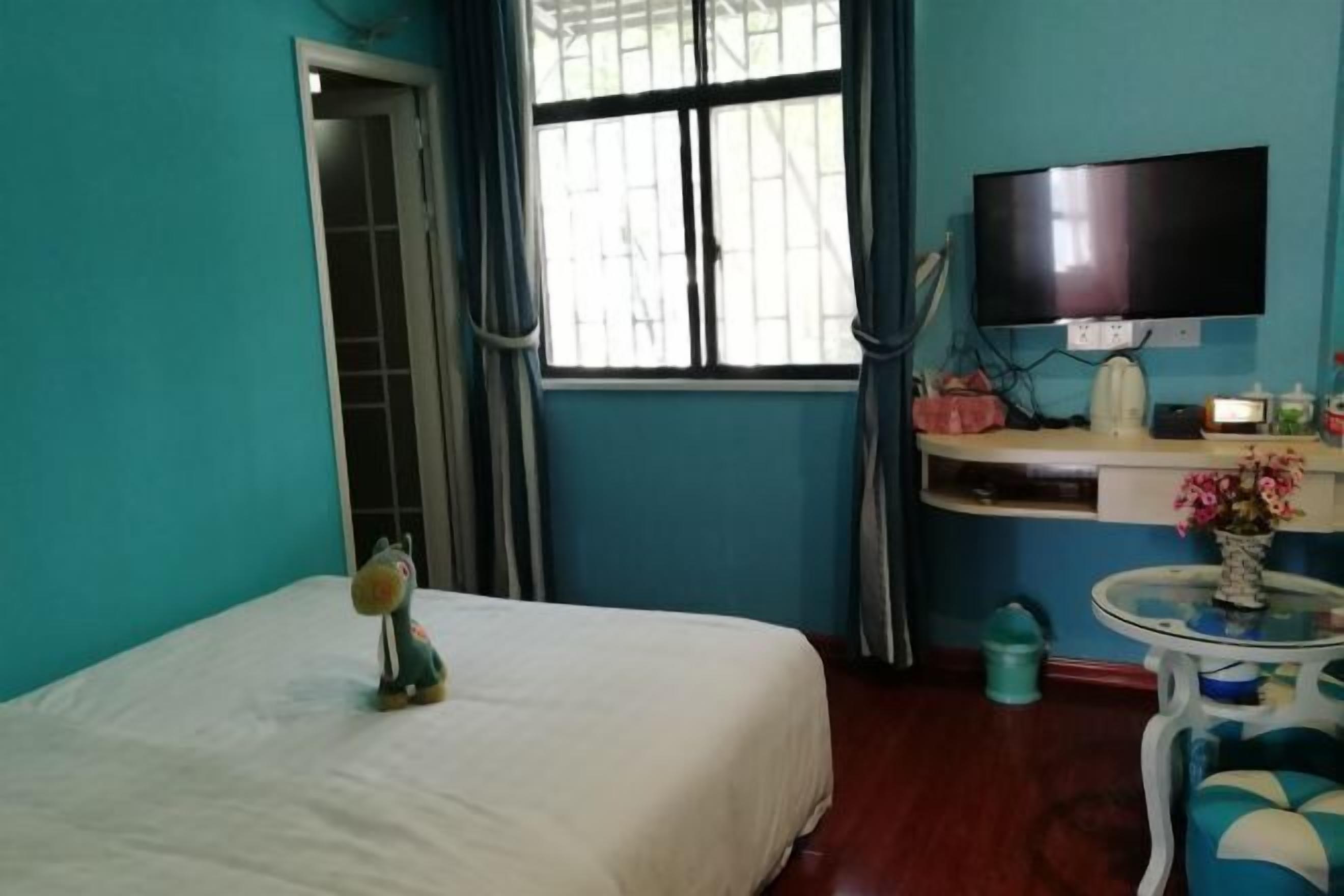 Une chambre avec un lit, un téléviseur fixé au mur, une petite table avec un vase et une fenêtre avec des rideaux.