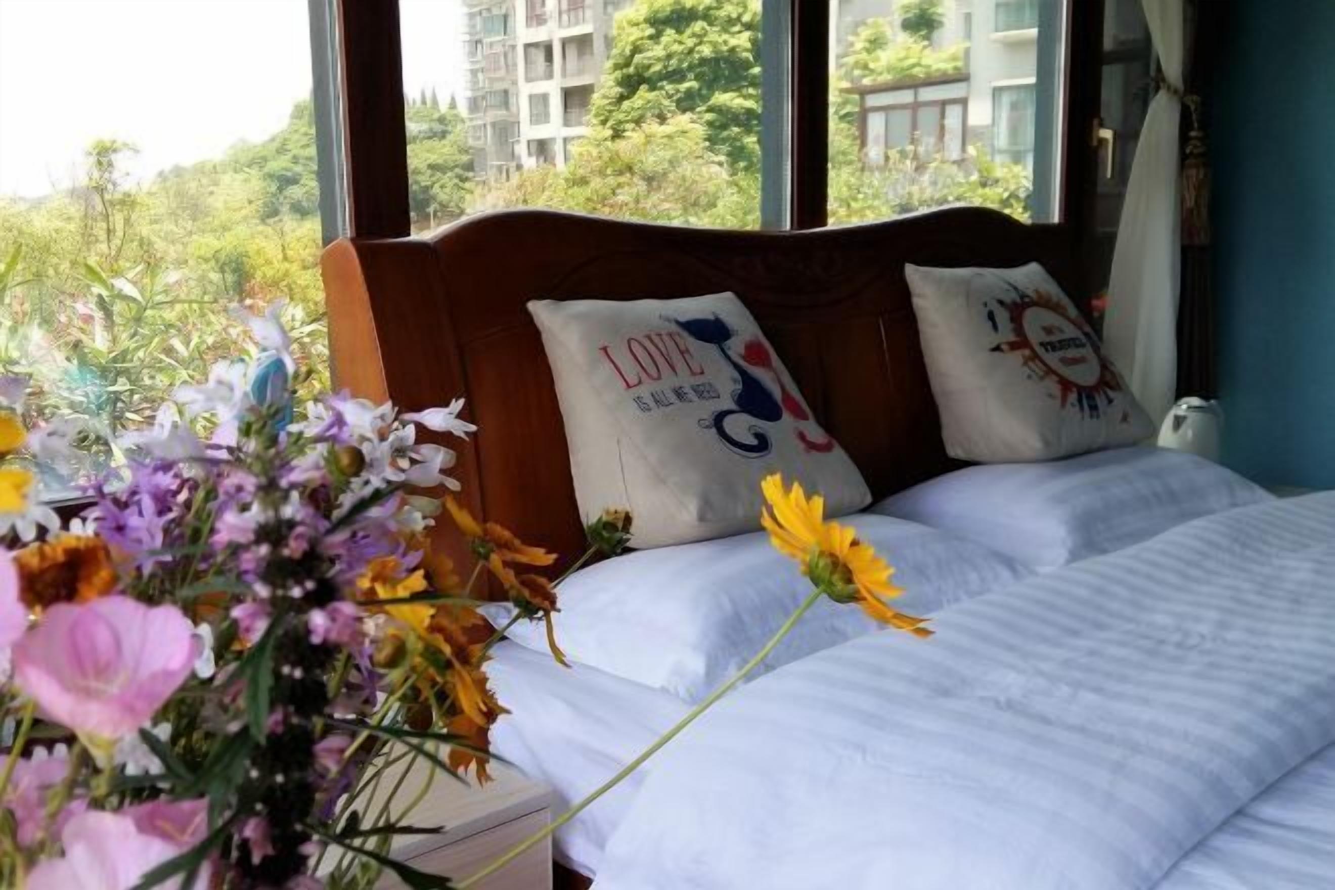 A bedroom with a wooden headboard, two pillows with text, a bed with white bedding, and a vase of flowers.