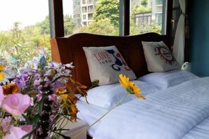 A bedroom with a wooden headboard, two pillows with text, a bed with white bedding, and a vase of flowers. - Deep Breathe Inn (Zixing)