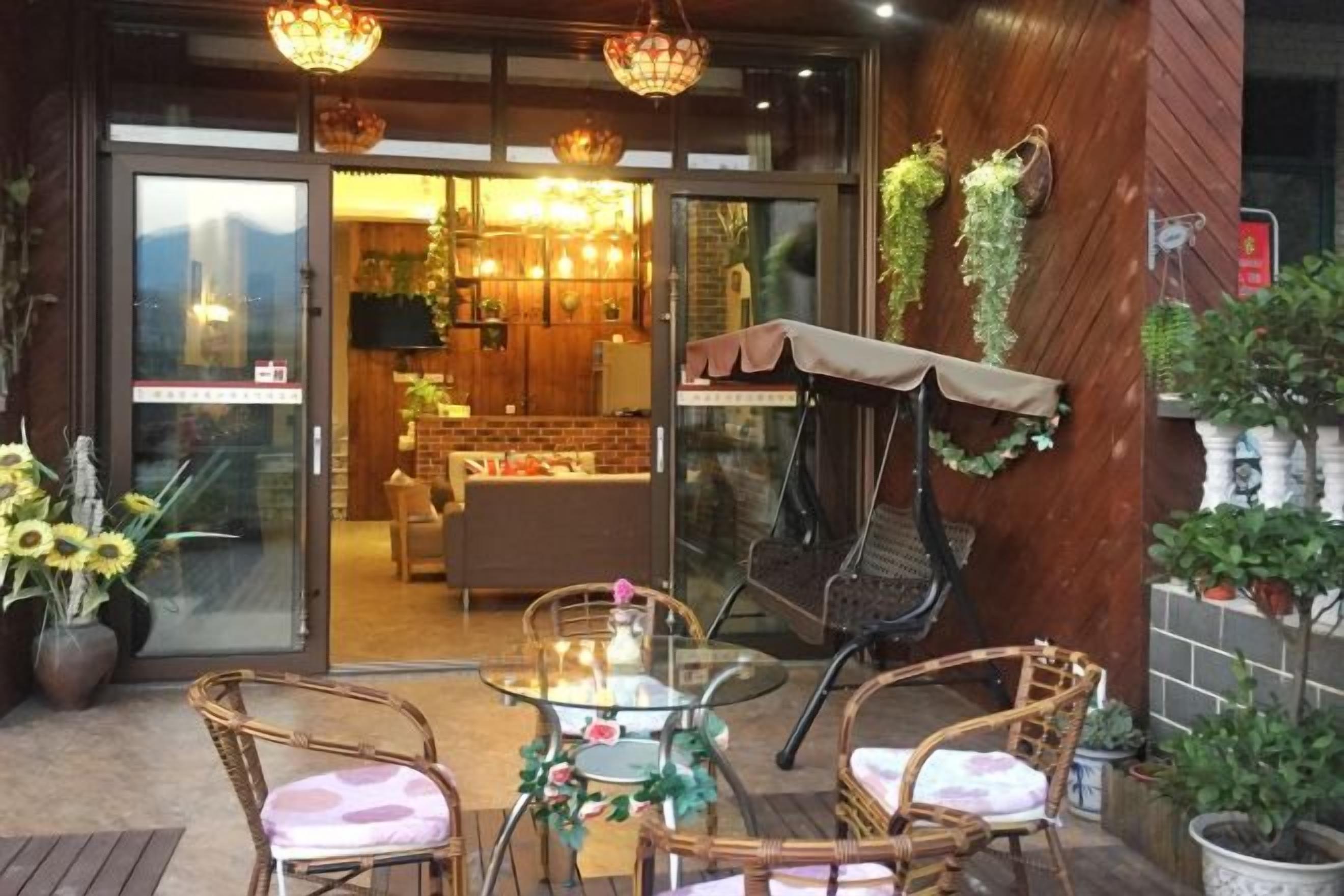 An outdoor seating area with wicker chairs and a glass table, a grill, and potted plants.