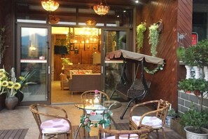 An outdoor seating area with wicker chairs and a glass table, a grill, and potted plants.