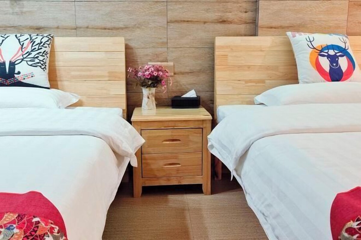 A hotel room with two beds, a wooden nightstand with a vase of flowers, and a small drawer.