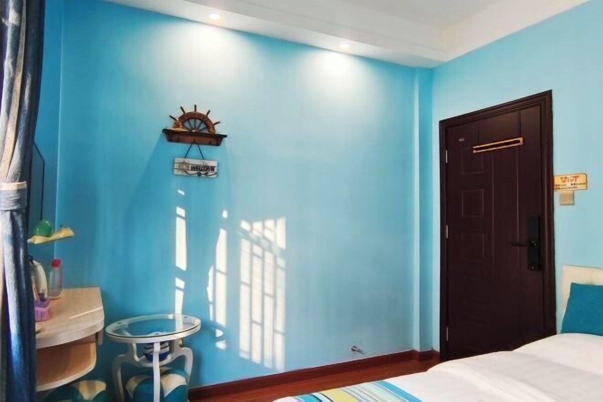 A room with a bed, a wooden door, a small table, and a wall-mounted shelf with a sign.