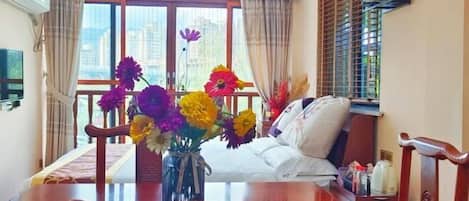 A hotel room with a dining table, chairs, a sofa, and a large window with curtains.