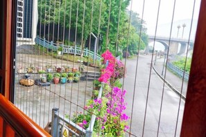 Vista a través de una ventana con baranda metálica, una calle con un puente y plantas en macetas.