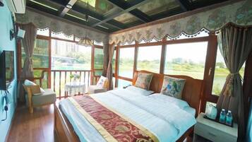 A bedroom with a large bed, a bedside table, a chair, and a window with a view of greenery.