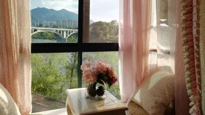 Une pièce avec une fenêtre, un vase de fleurs et une vue sur un pont et des montagnes.