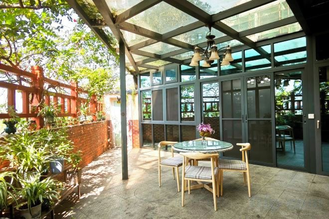 An outdoor patio with a glass enclosure, a round table with chairs, and potted plants.