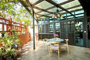 Un patio exterior con cerramiento de vidrio, una mesa redonda con sillas y plantas en macetas.
