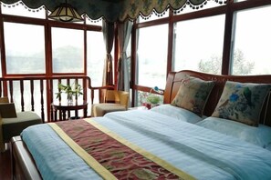 A bedroom with a large bed, a wooden headboard, a small table, and a chair. There is a window with curtains and a view of the outdoors. - Deep Breathe Inn (Zixing)