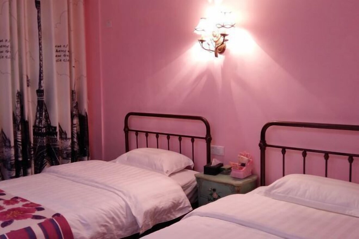 A bedroom with two beds, a nightstand, and a wall-mounted lamp.