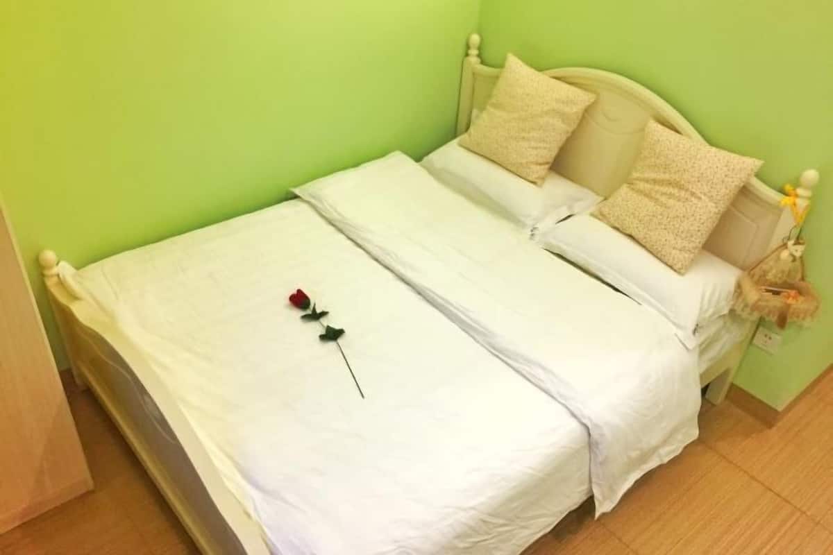 A single-bed room with a green wall, white bedding, and a rose on the bed.