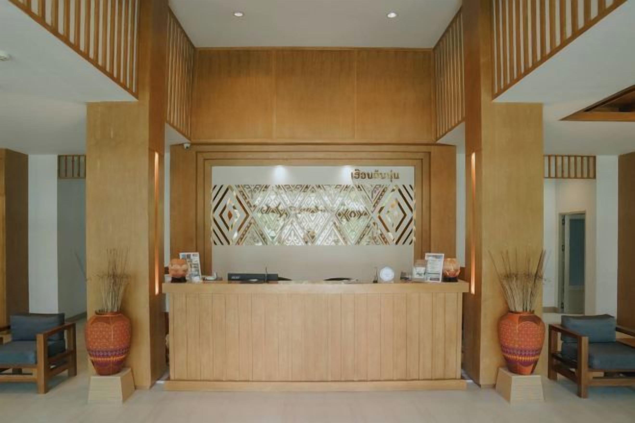 A reception desk with a decorative back panel, two potted plants, and a seating area with chairs.