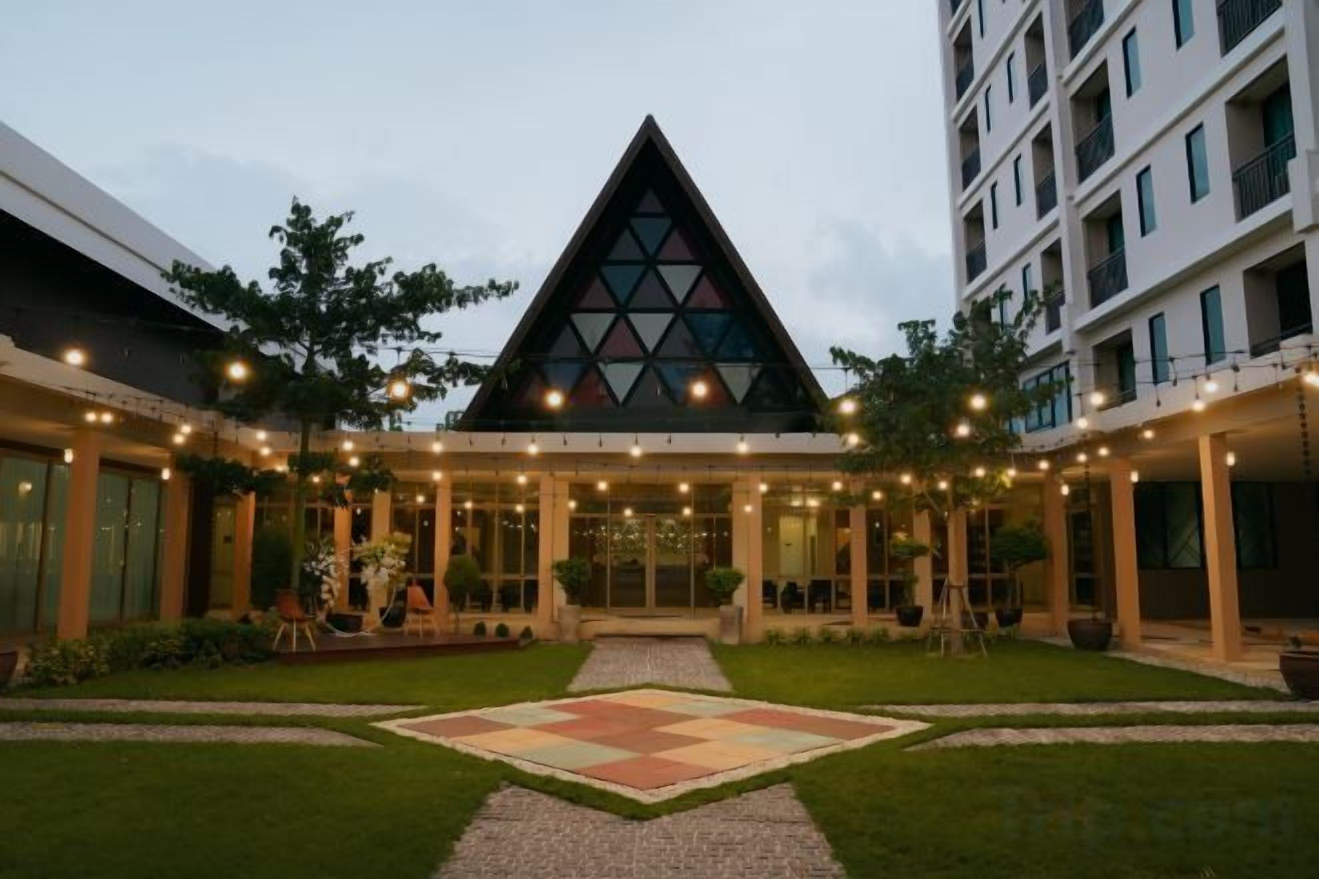 Un hotel con un atrium central, una estructura de cristal triangular y un patio con un área de diseño geométrico.