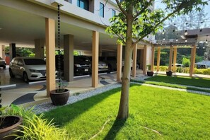 A covered parking area with multiple cars, a well-maintained lawn, and a potted plant. - The Cotton Tree Hometel (Khon Kaen)