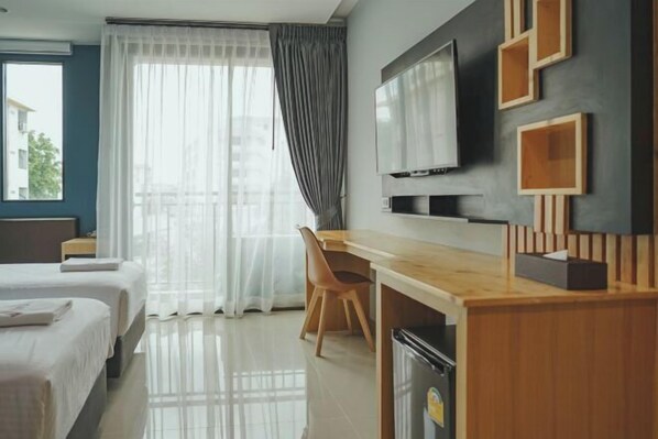 Habitación de hotel con dos camas, un escritorio de madera, televisión y vistas a la ciudad a través de amplios ventanales.