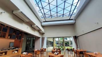 A spacious indoor area with a high ceiling and a skylight, featuring tables and chairs arranged for dining.