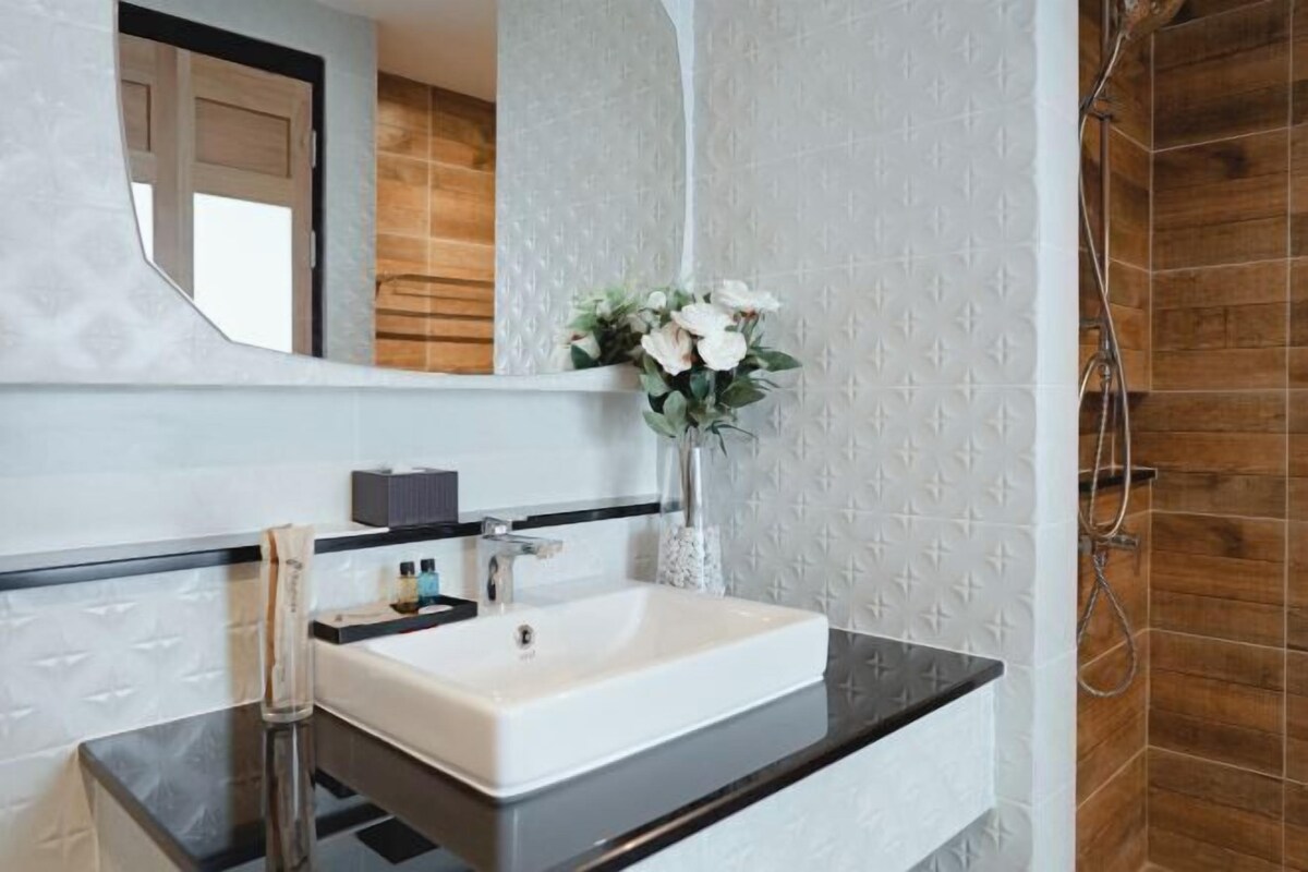 Ein Badezimmer mit einem weißen Waschbecken, einem Spiegel, einer Vase mit Blumen und einer Duschkabine.