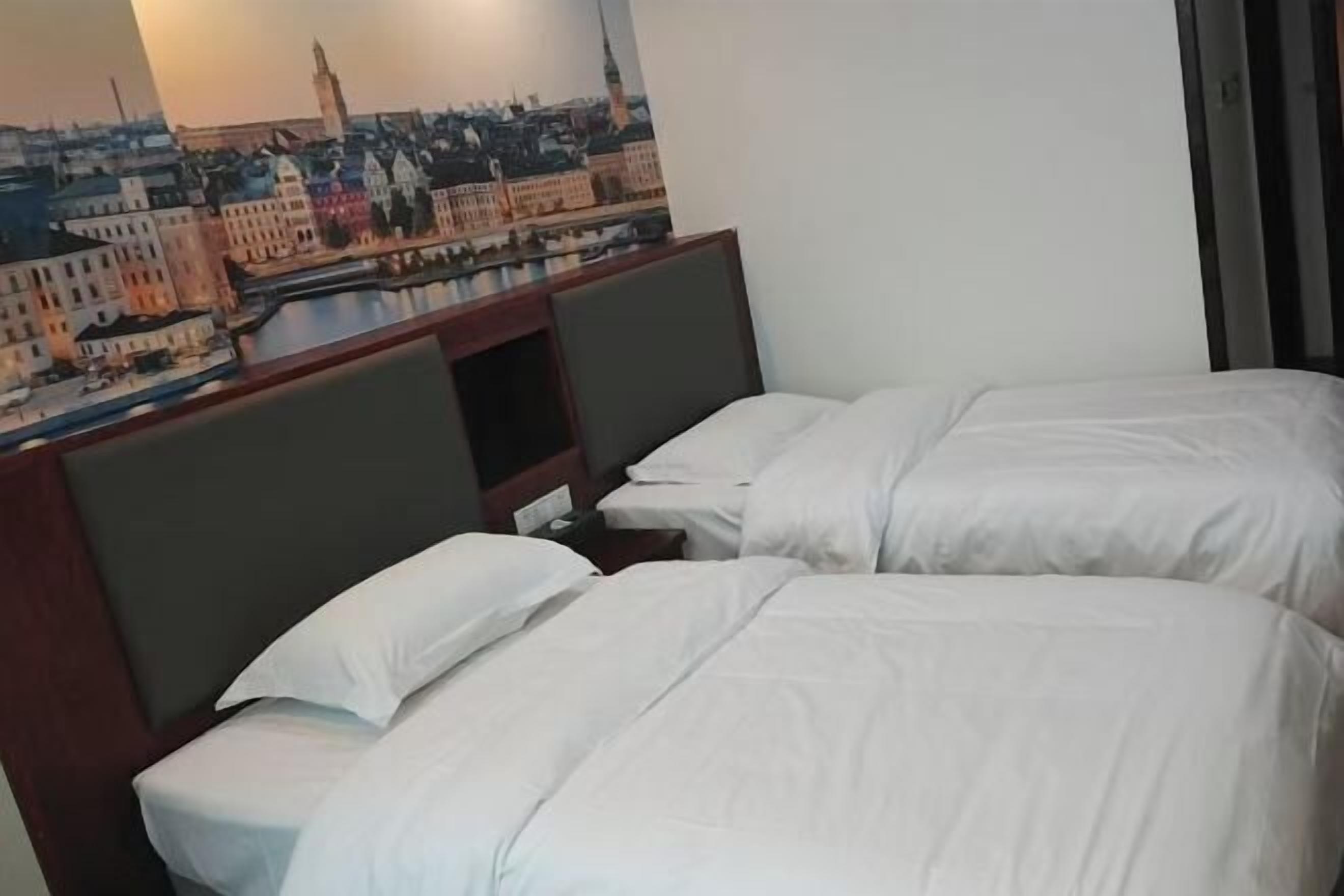 Una habitación de hotel con dos camas individuales, cabecera con un mural de paisaje urbano y ventana con vista a edificios.