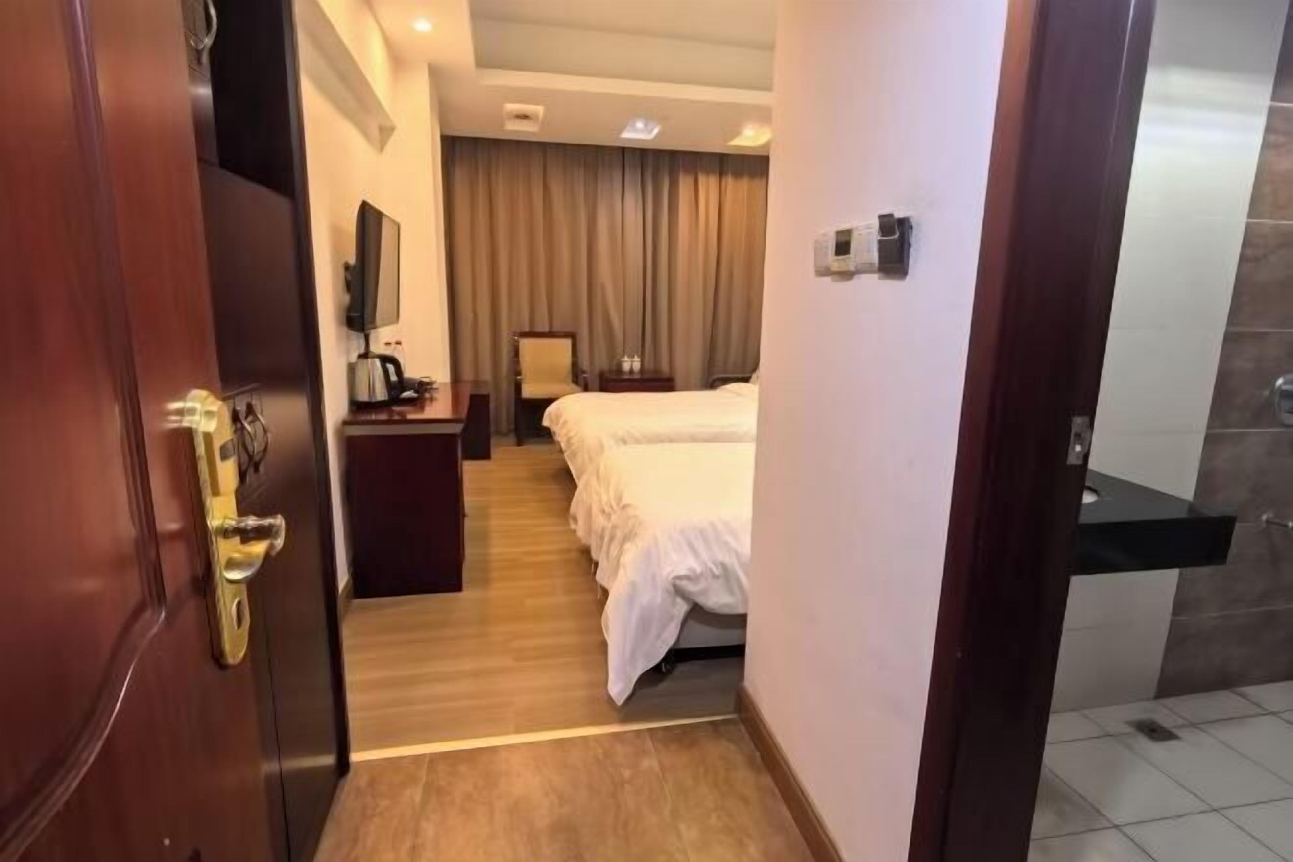 Una camera d'albergo con una porta in legno, un letto, una scrivania con una sedia, una televisione e un bagno con doccia.