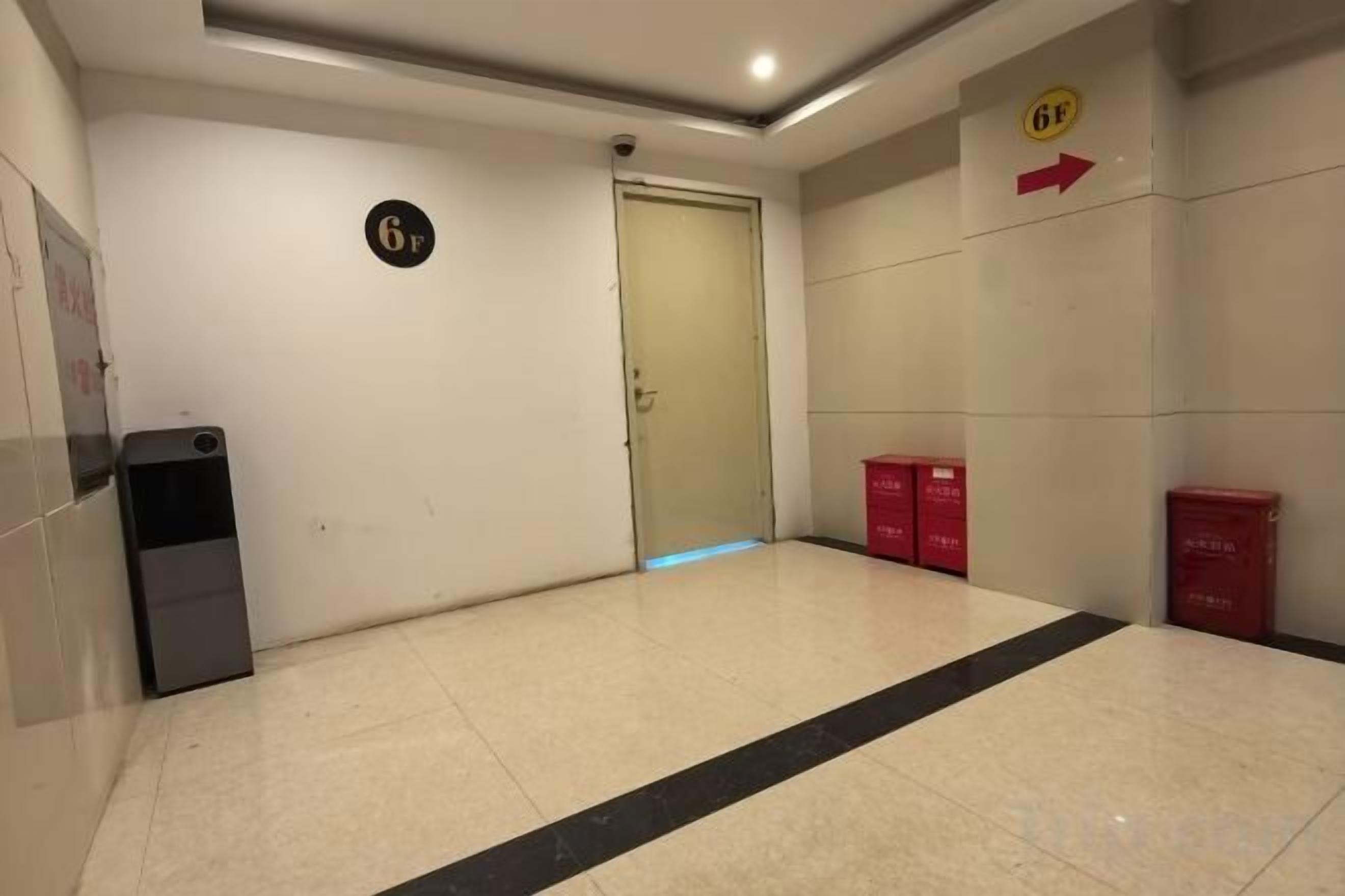 Un couloir avec une porte portant l’inscription « 6F », une poubelle et des boîtes rouges sur le côté droit.