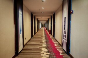 A hotel corridor with a carpeted floor, doors on both sides, and a red carpet runner.