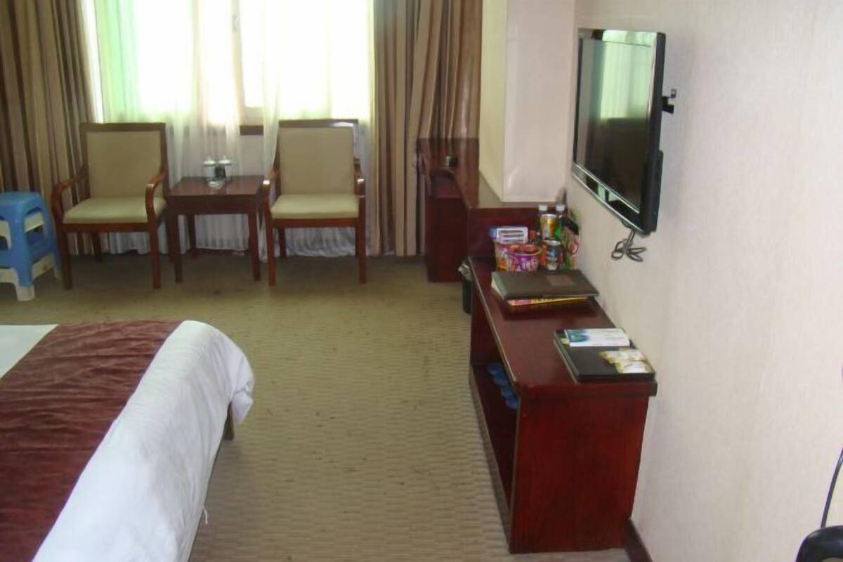 A hotel room with a bed, a desk with a TV, two chairs, and a small table with a lamp.