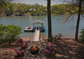 A lakeside deck with a fire pit, outdoor seating, and a dock extending into the water.